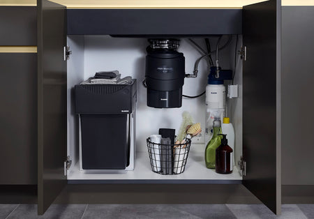 Black waste disposal unit in open under-sink cabinet with side access doors