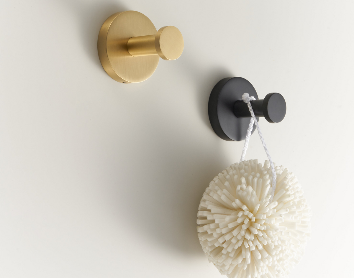 Brushed brass wall hook with dark accessory holder and hanging sponge