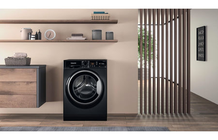 Hotpoint black freestanding front-load washing machine standing in a laundry room