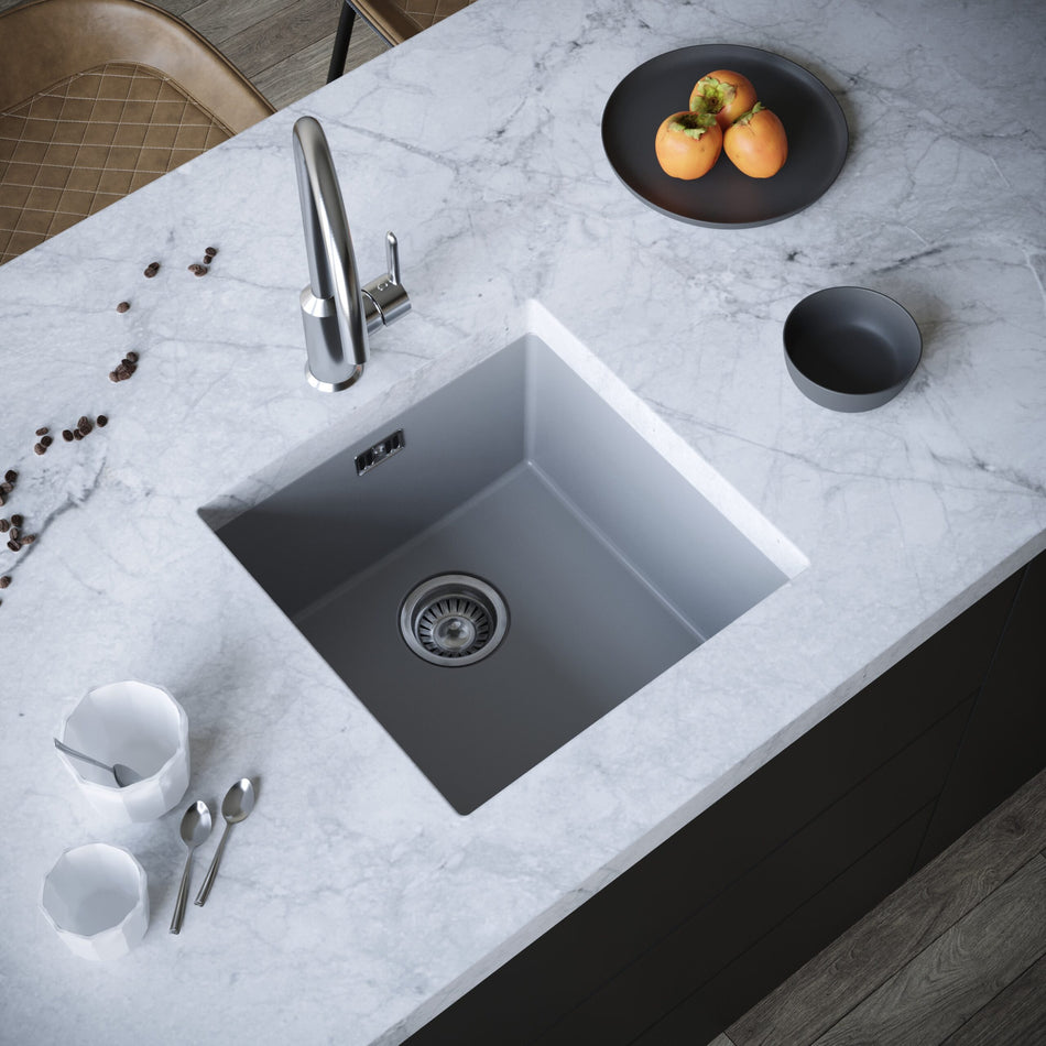 Square single-bowl kitchen sink in dark gray, showing faucet opening and drain