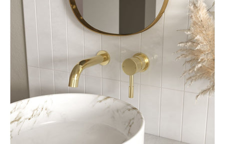 Brushed brass wall-mounted bath/shower mixer with handheld shower head above sink