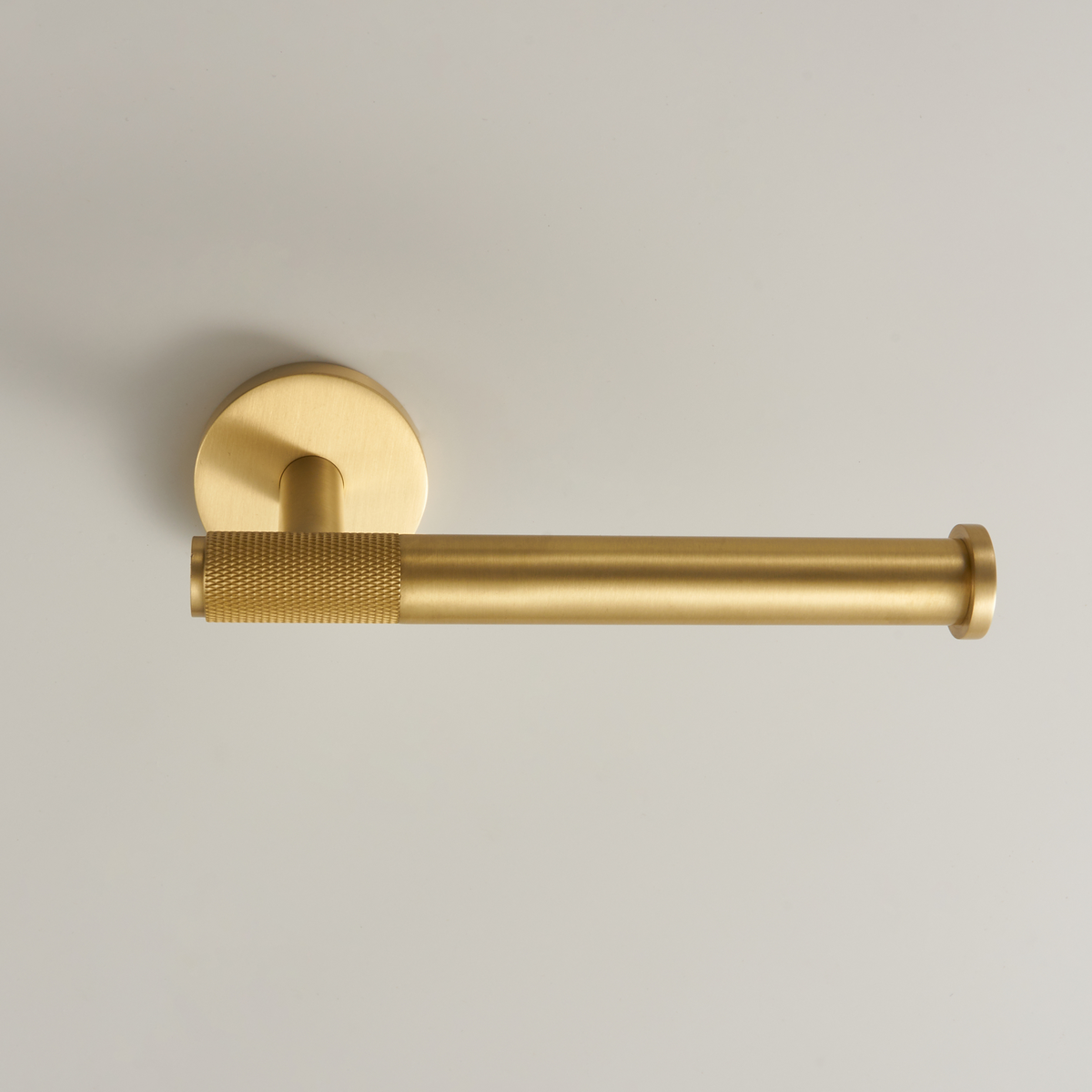 Brushed brass toilet roll holder with round wall plate and textured metal grip