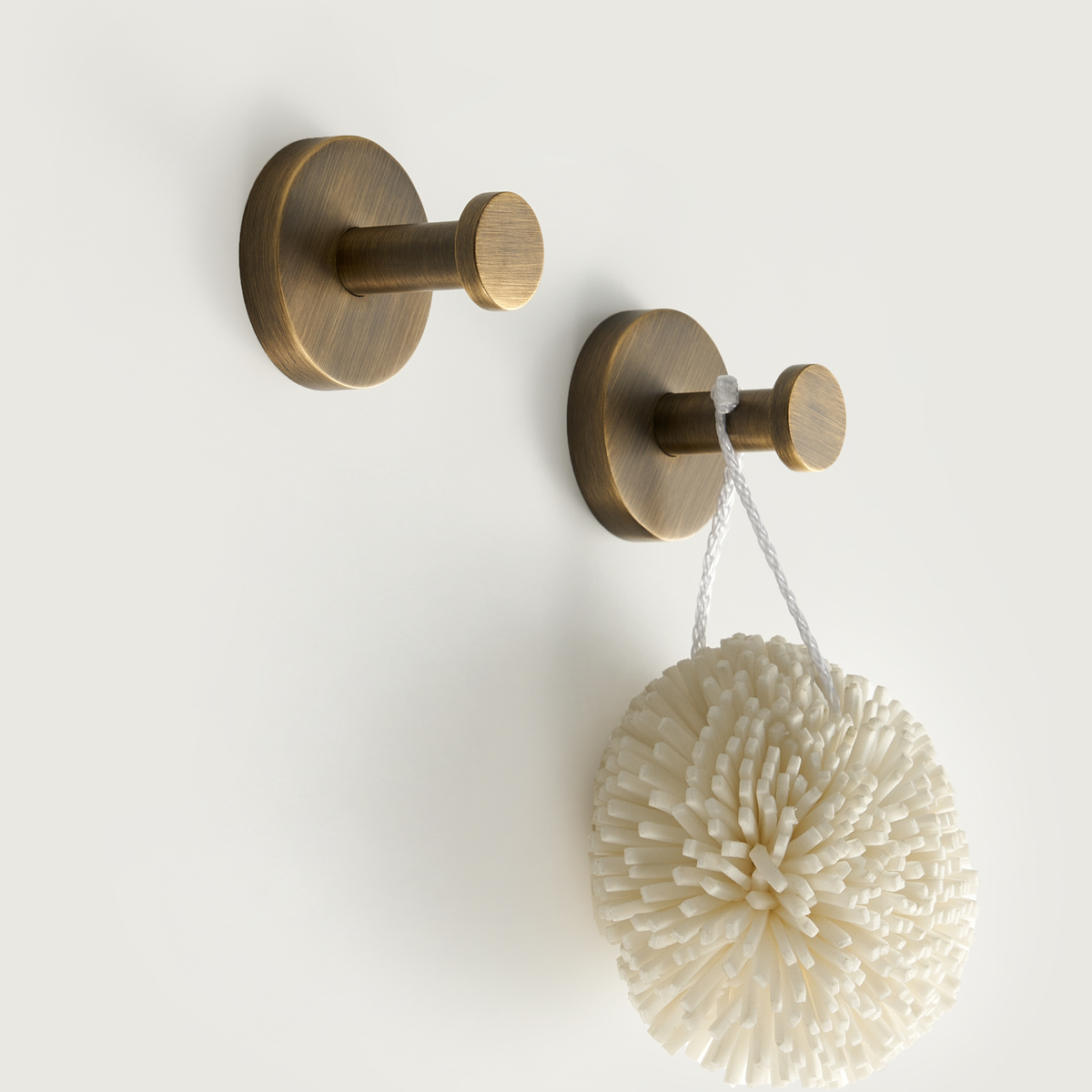 Brushed brass hook set with round bases holding a white textured bath puff