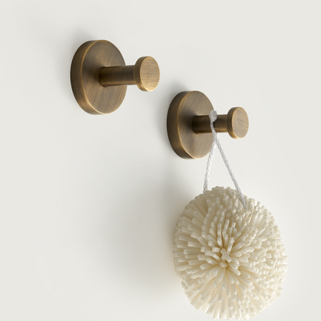 Brushed brass hook set with round bases holding a white textured bath puff