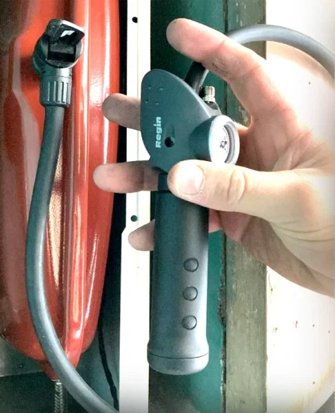 Gray hand pump with pressure gauge and connected hose for system top-up